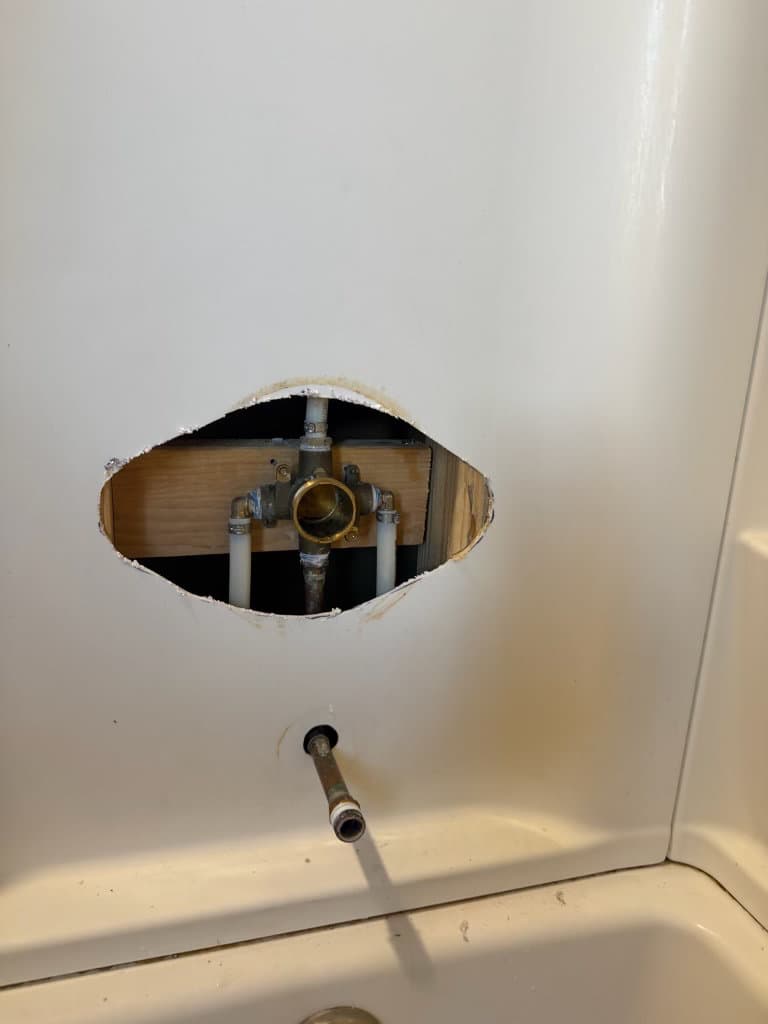 Before: access hole in shower surround showing old plumbing valve rough-in — Oopsie Daisy Plumbing bathroom plumbing repair, Northern Colorado